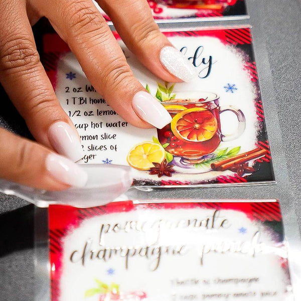 Hands holding UV DTF stickers for a festive drink recipe, showcasing vibrant colors and design details.