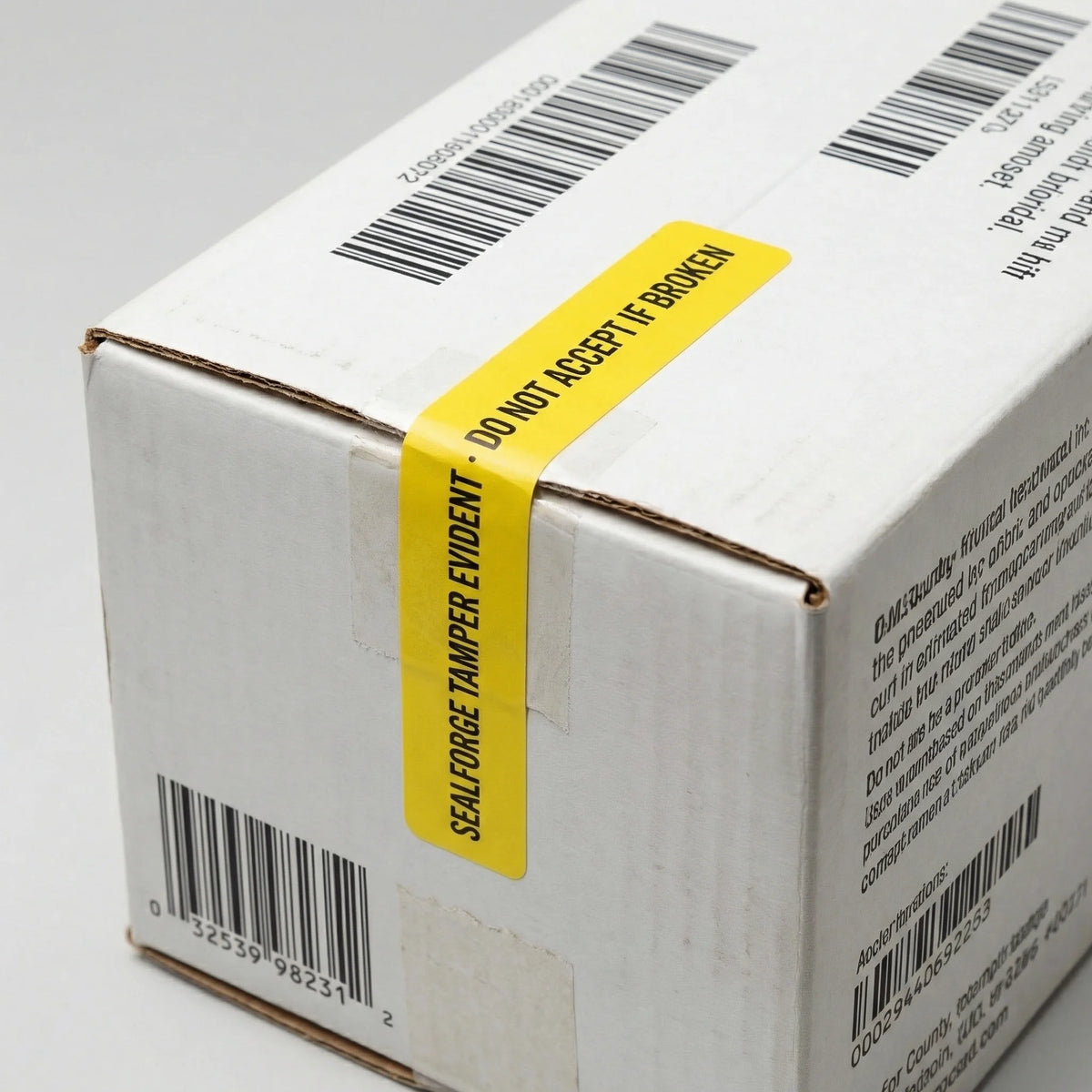 White box with yellow tamper evident label and barcodes on a gray background