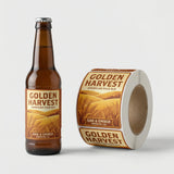 Brown beer bottle with 'Golden Harvest' label and a roll of labels on a light gray background
