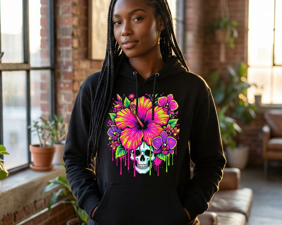 Person wearing a black hoodie with a colorful skull and flower design in a room with large windows and plants.