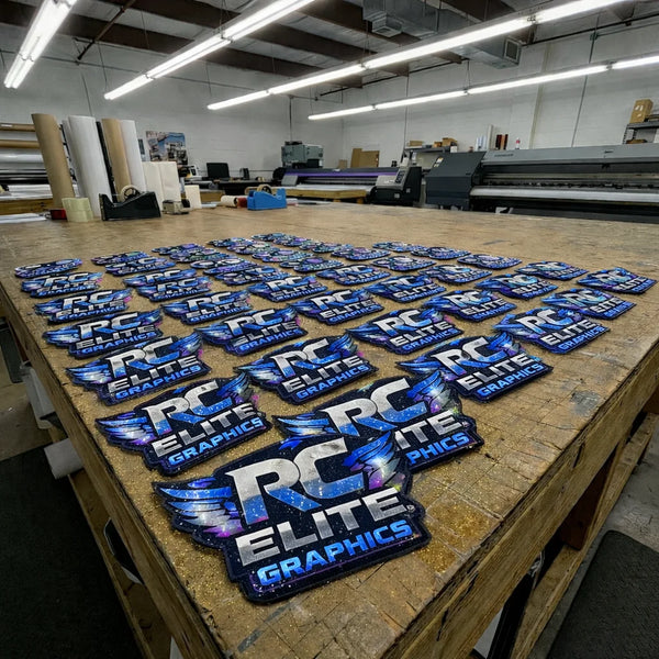 Table with multiple 'RC Elite Graphics' branded patches in a workshop setting